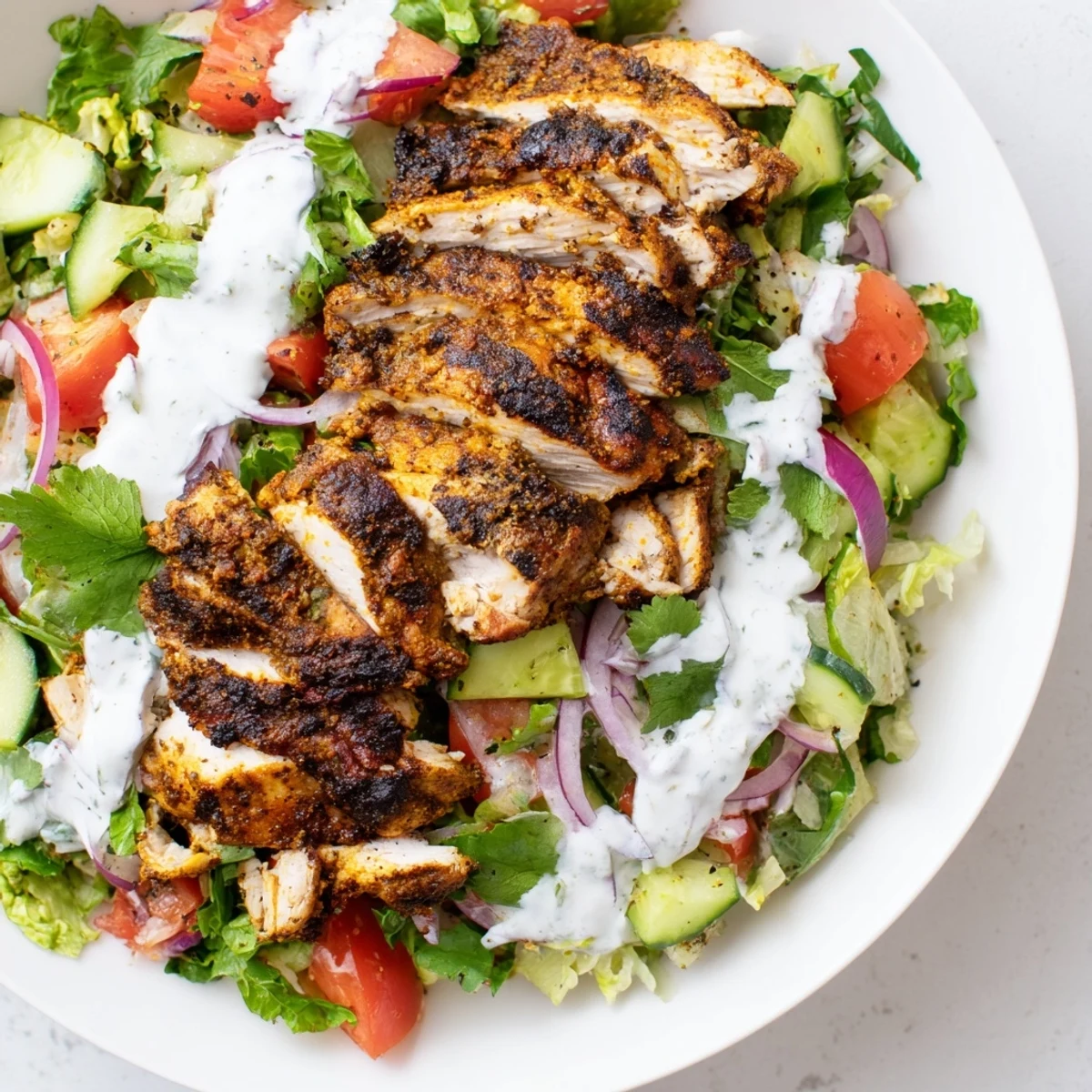 Sliced, charred chicken shawarma crowns a fresh salad of cucumbers, tomatoes, and onions, finished with a drizzle of yogurt dressing.