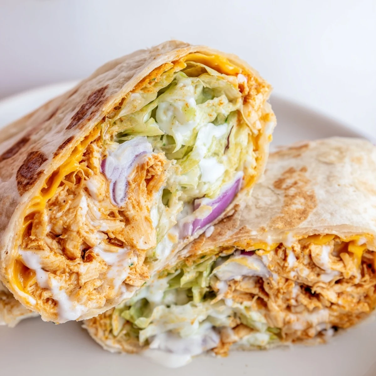 Four cut Buffalo Ranch Chicken Wraps arranged on a wooden board, drizzled with extra ranch and buffalo sauce, ready to serve.