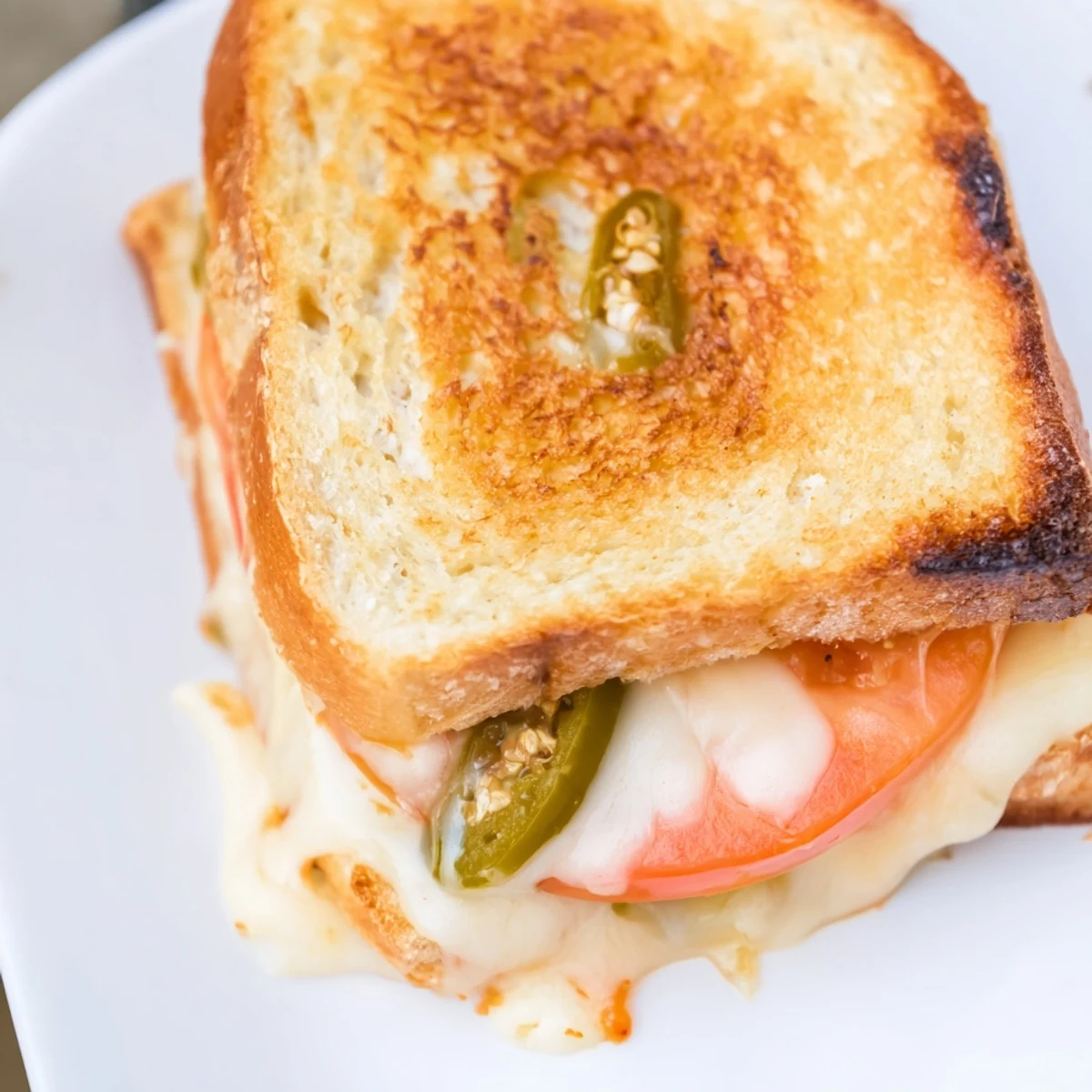 A spicy Pepper Jack & Tomato Grilled Cheese rests beside fresh tomato slices and a creamy dipping sauce on a wooden board.  