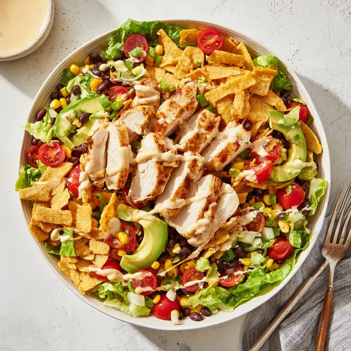 A close-up of Crunchy Taco Chicken Salad featuring seasoned chicken, black beans, corn, cheese, and diced avocado on romaine lettuce.