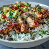 A steaming Cajun Chicken Bowl features sliced avocado and fresh cilantro, served with lime wedges for a bright finish.