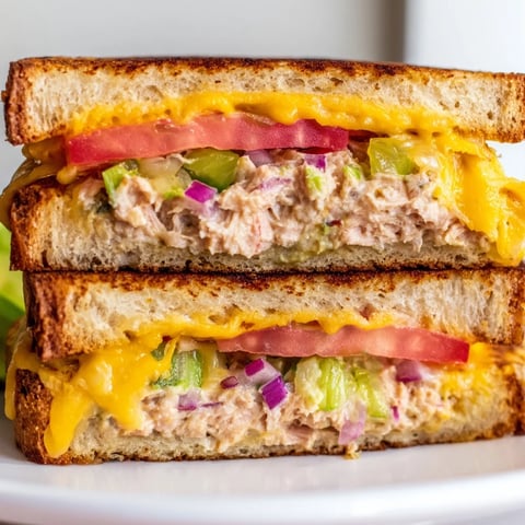 Golden brown sourdough slices overflowing with spicy tuna melt, melted cheddar cheese, and fresh tomato on a rustic plate.
