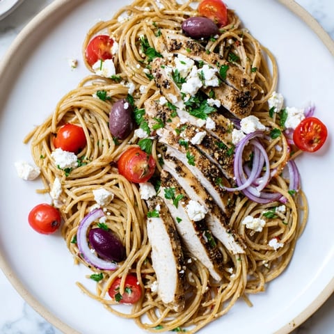 A vibrant serving of Greek Chicken Spaghetti with juicy grilled chicken, halved cherry tomatoes, and crumbled feta on a plate.