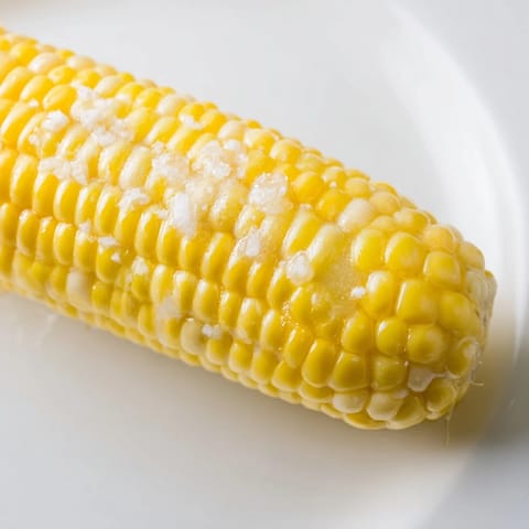 Grilled corn on the cob, with smoky char marks, ready to be slathered in butter and served hot.