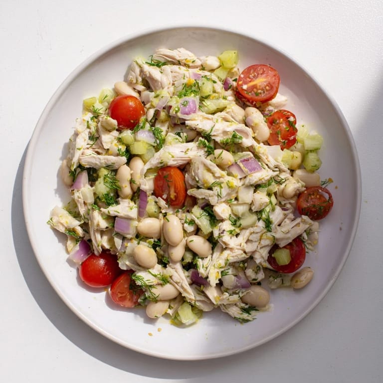 A close-up of Lemony White Bean Chicken Salad shows shredded chicken and white beans glistening with a tangy lemon herb dressing.