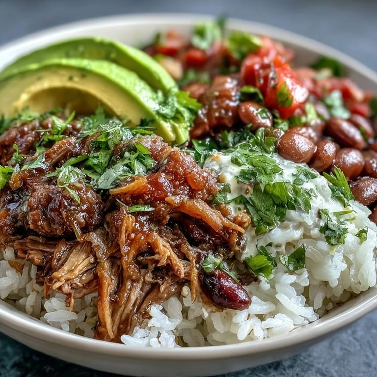 A hearty, gluten-free Mexican-style bowl featuring slow-cooked pork, pinto beans, and lime wedges ready for squeezing.
