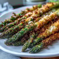 Golden-baked Crispy Asparagus Asiago Spears with a crunchy panko crust, served with lemon wedges on a white plate.